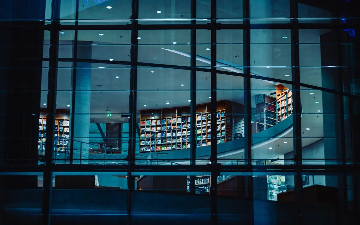 Library bookshelves seen through a glass wall at night